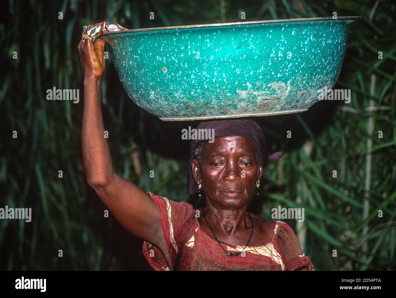 Ouassou, Ivory Coast, Cote d'Ivoire. Elderly Ivorian Woman Carrying Basin on Head. Stock Photo