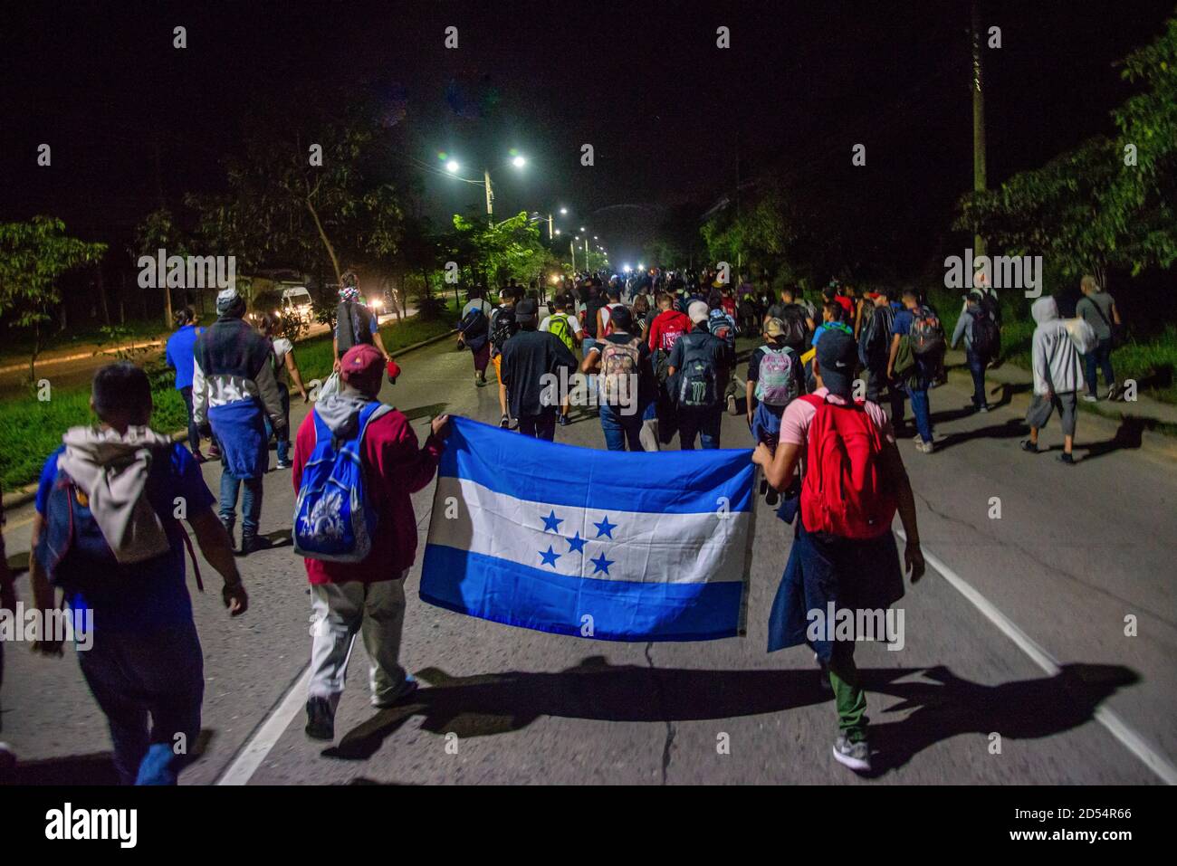 San Pedro Sula, Honduras. 15th Jan, 2020. Migrants march with a Honduran flag walking towards the Guatemalan border at 4am on the first day of their journey to the U.S. border. Migrants are fleeing from extreme poverty and gang violence, hoping to find a better life in the U.S. They must travel over 3,000 miles through Guatemala and Mexico, often times with nothing but the clothes on their back, to reach the border in Tijuana, Mexico where their fate is undecided. Credit: Seth Sidney Berry/SOPA Images/ZUMA Wire/Alamy Live News Stock Photo