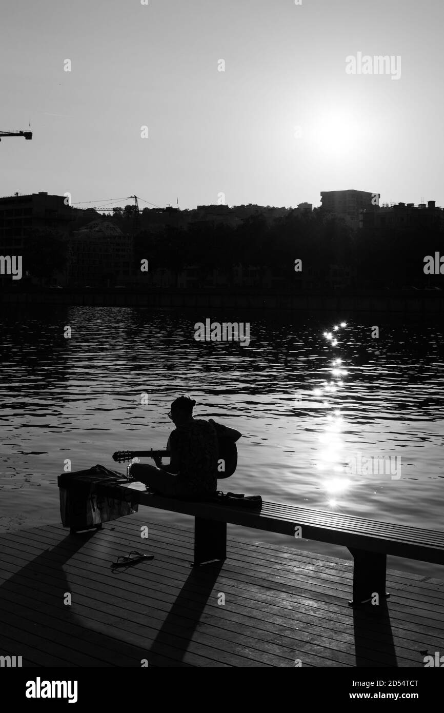 Vertical grayscale shot of a lonely person sitting by the lake at sunset Stock Photo