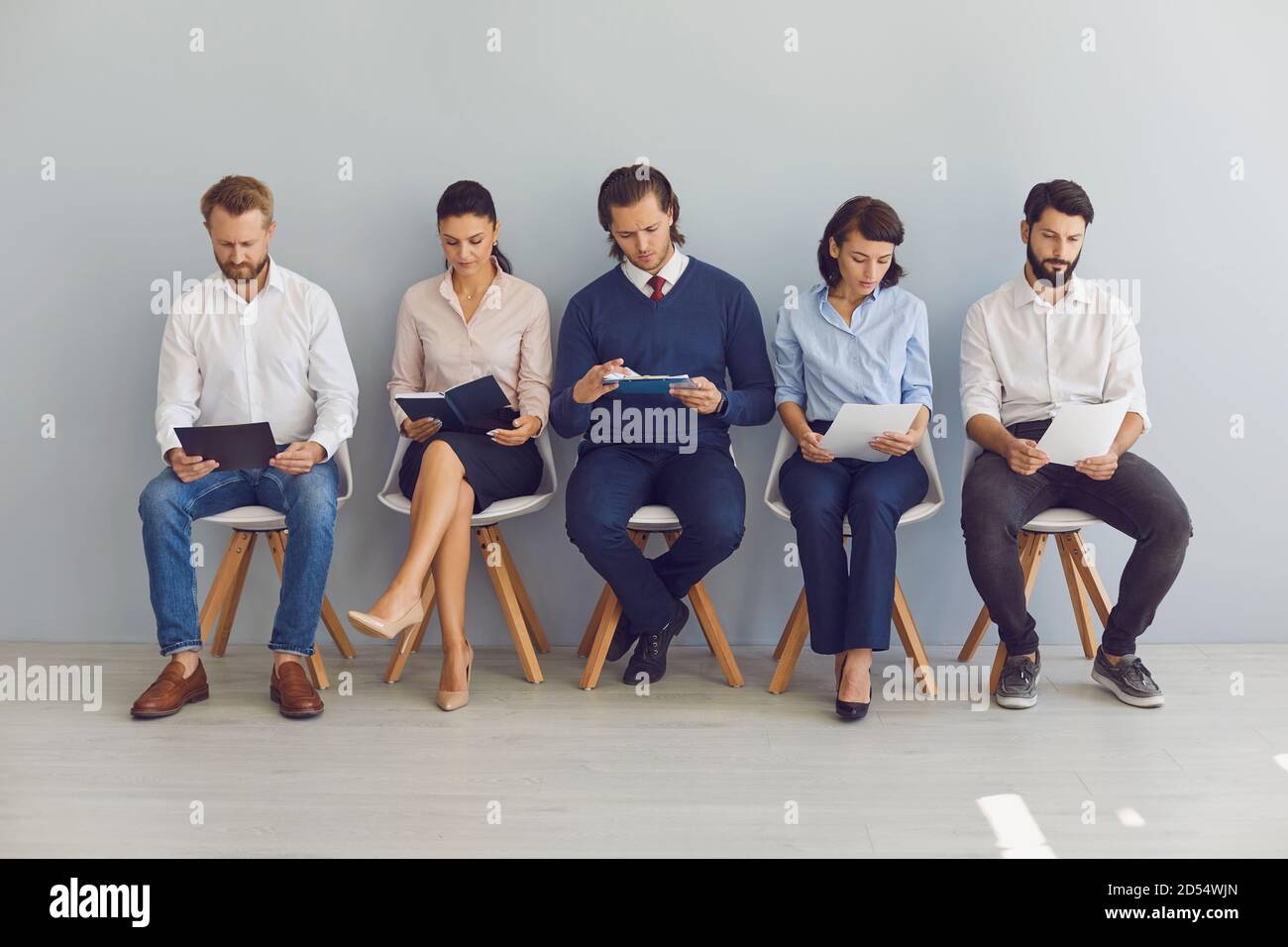 Job seekers with resumes in hands waiting for job interview sitting on chairs in a row Stock Photo