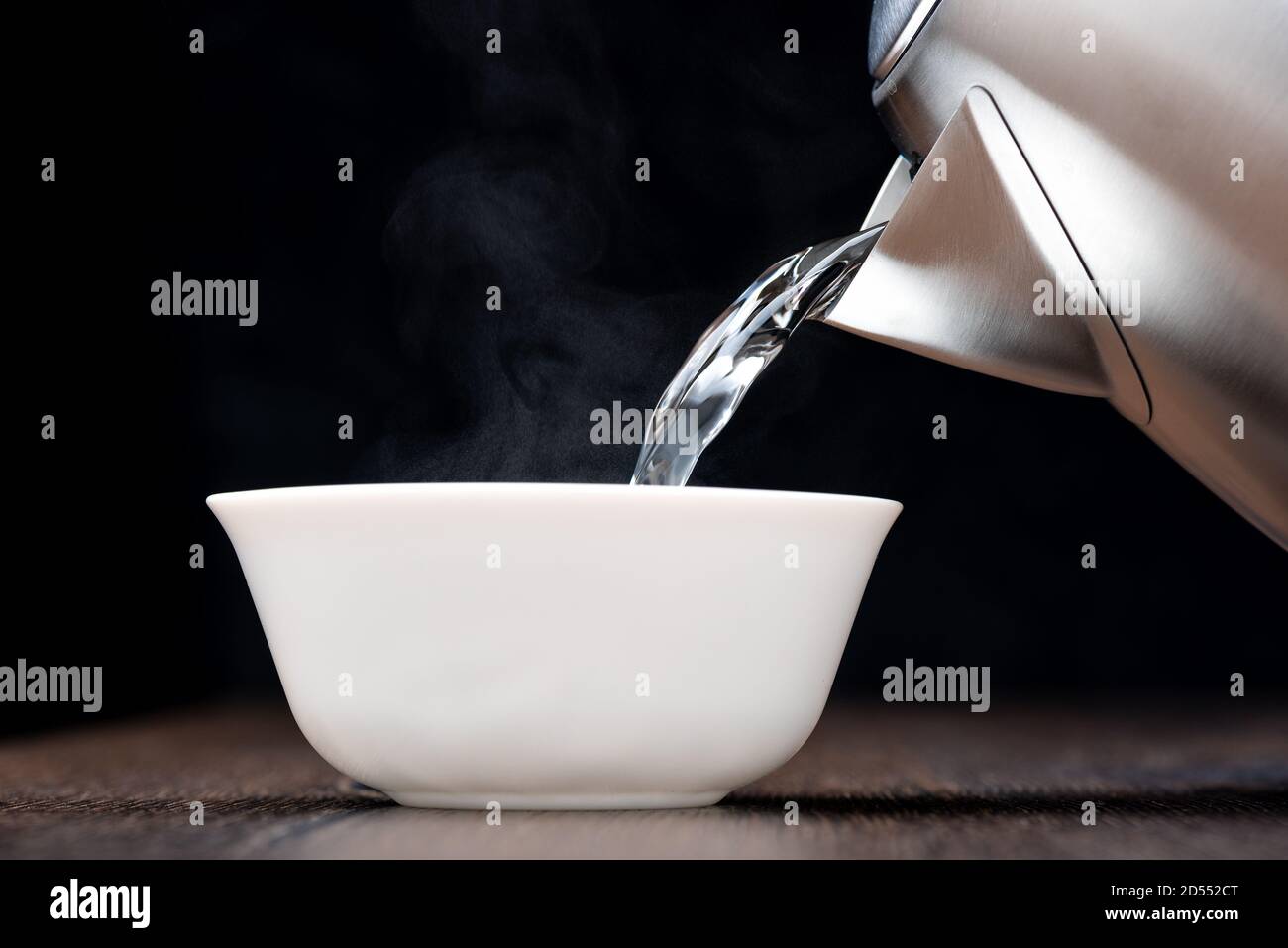 Pouring hot boiling water into a white bowl. Steam on a dark background