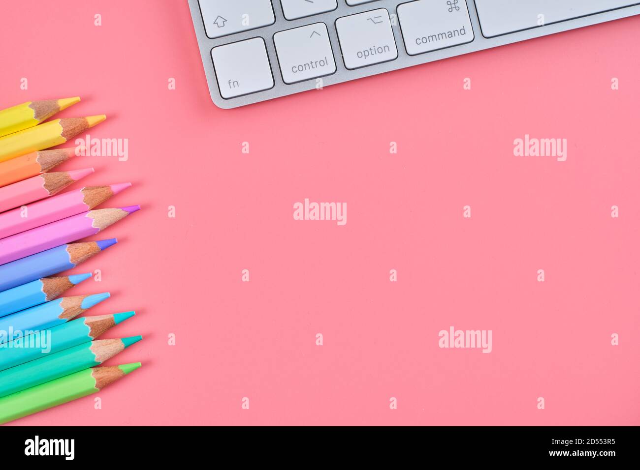 Top view of a keyboard and colored pencils on a pink background with ...