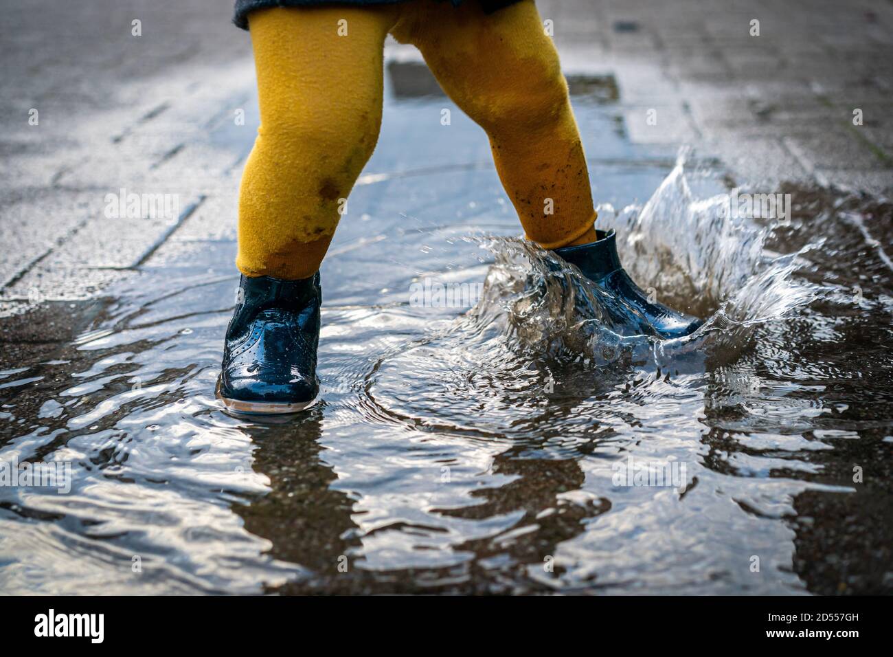 October 7th, 2020, Trebbin, a little girl with rubber shoes and yellow tights jumps around in a puddle and has a lot of fun. | usage worldwide Stock Photo
