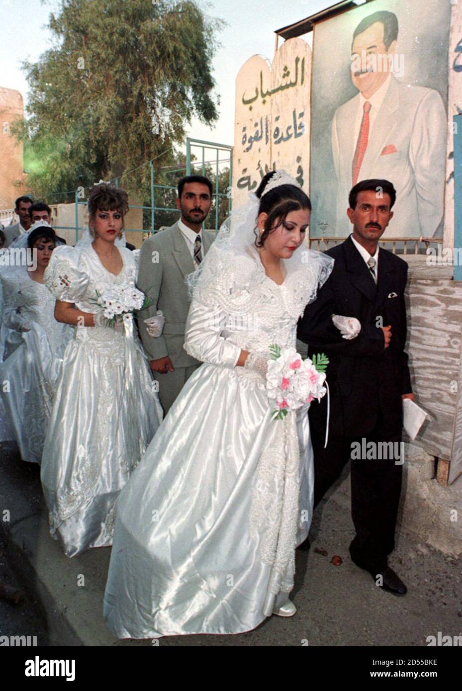 Brides and grooms walk past a portrait of Iraqi President Saddam Hussein August 9. Some 112 couples got married on Monday in an event prepared and paid for by the Iraqi youth Association, a body chaired by President Saddam Hussein's elder son. Stock Photo