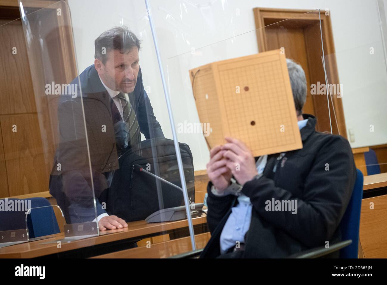 Oldenburg, Germany. 13th Oct, 2020. The accused, who hides his face with a folder, sits in handcuffs in the courtroom before the murder trial begins and talks to his lawyer Stefan Hoffmann. The 51-year-old man is said to have murdered his partner in an insidious manner in June 2020 in Ganderkesee in the Oldenburg district. Credit: Sina Schuldt/dpa/Alamy Live News Stock Photo