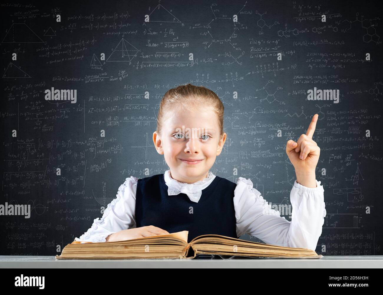 Smiling little girl sitting at desk with open book Stock Photo - Alamy