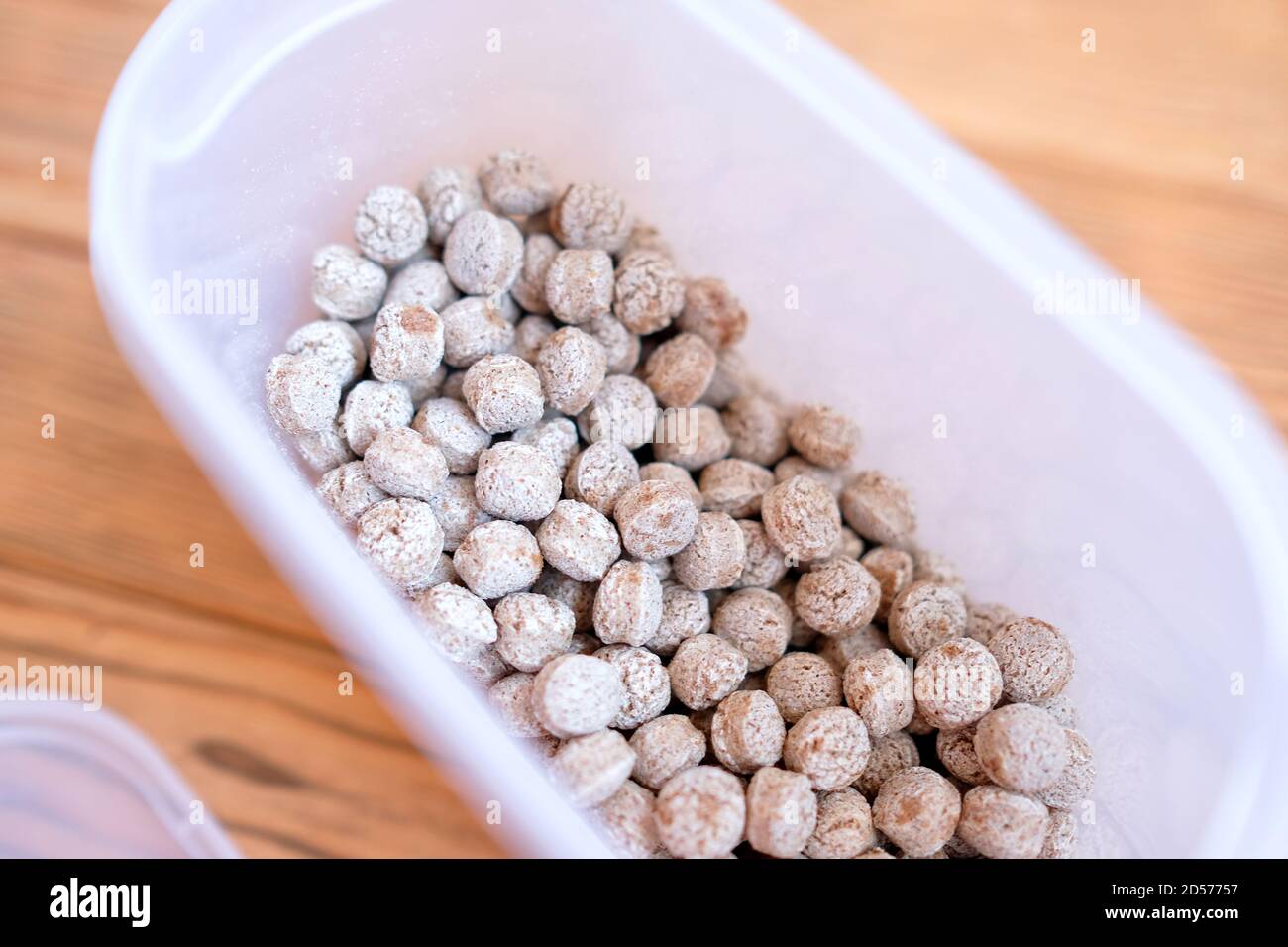 Bran in a plastic container. Dry edible balls. Wood background. Stock Photo