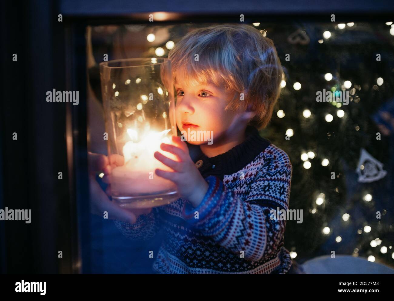 Portrait of small boy indoors at home at Christmas, holding candle at night. Stock Photo