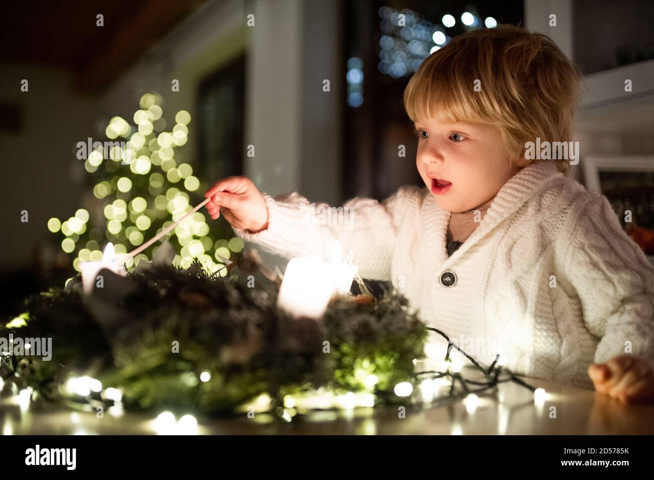 Portrait of small boy indoors at home at Christmas, lightning candles. Stock Photo