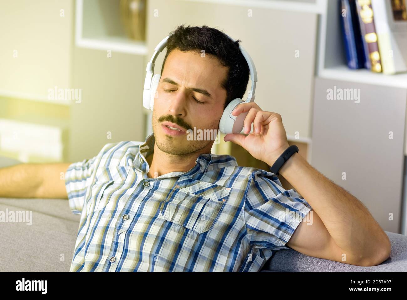 Blissful young man listening to music on stereo headphones as he relaxes on a sofa at home with eyes close immersed in the soundtrack Stock Photo