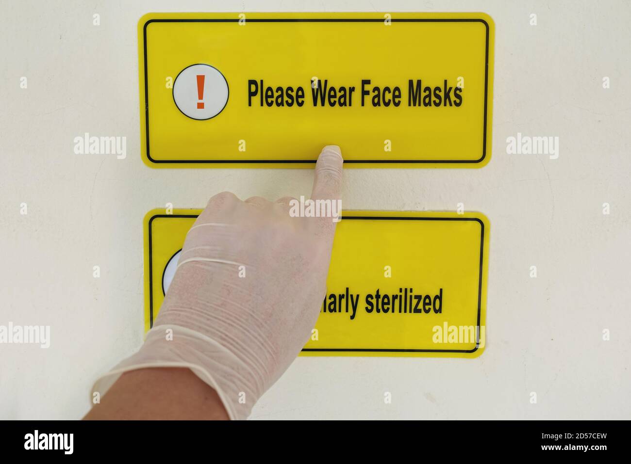 Hand in plastic glove pointing to sign urging to wear face mask. Stock Photo