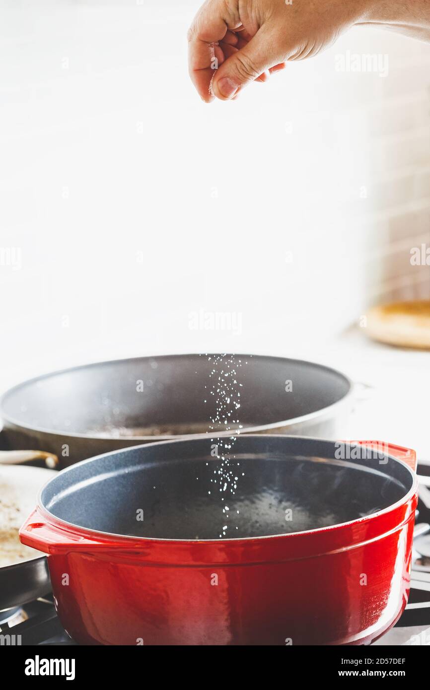 Man's hand adding salt while cooking food in a red enameled cast iron