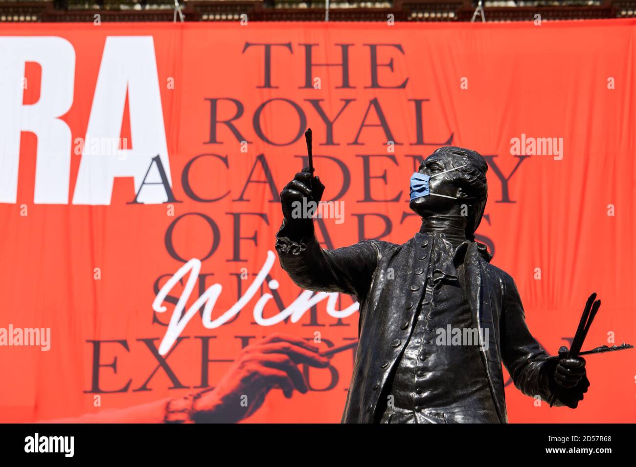 London, UK. - 5 Oct 2020: A masked statue in front of a banner advertising the traditional Royal Academy Summer Exhibition, delayed until October due to the coronavirus pandemic. Stock Photo