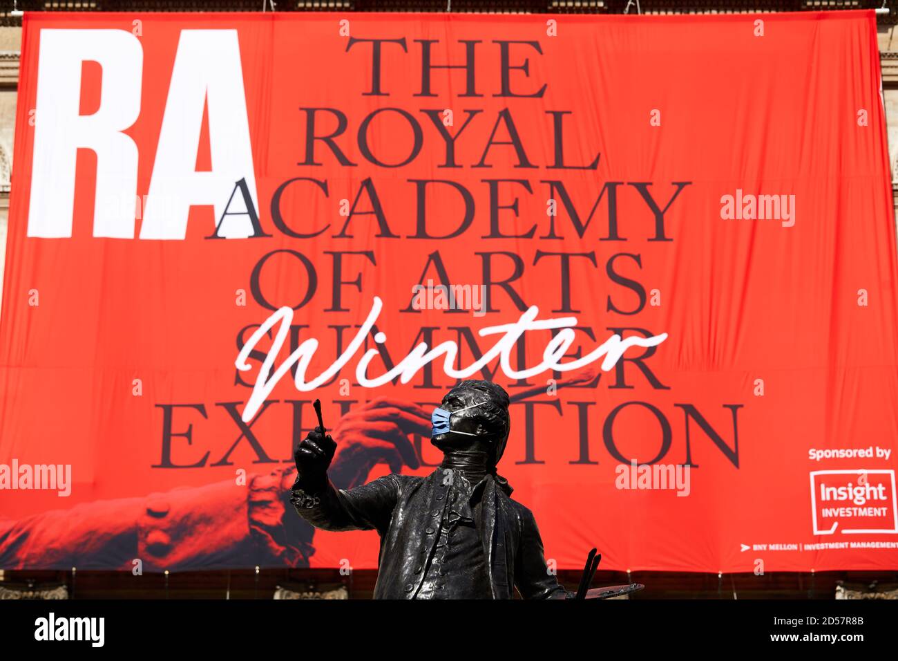 London, UK. - 5 Oct 2020: A masked statue in front of a banner advertising the traditional Royal Academy Summer Exhibition, delayed until October due to the coronavirus pandemic. Stock Photo