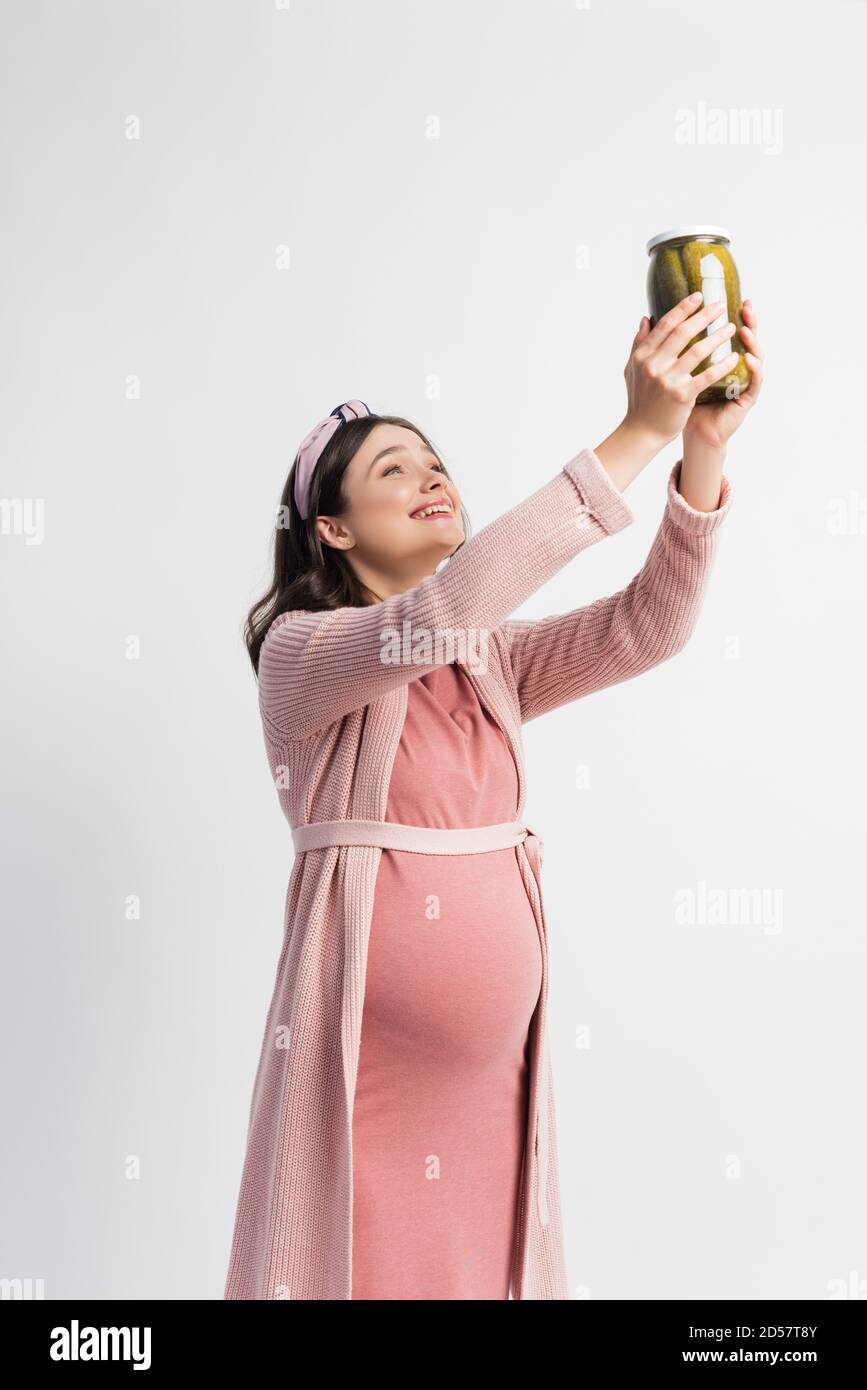 pleased and pregnant woman holding jar with pickled cucumbers above