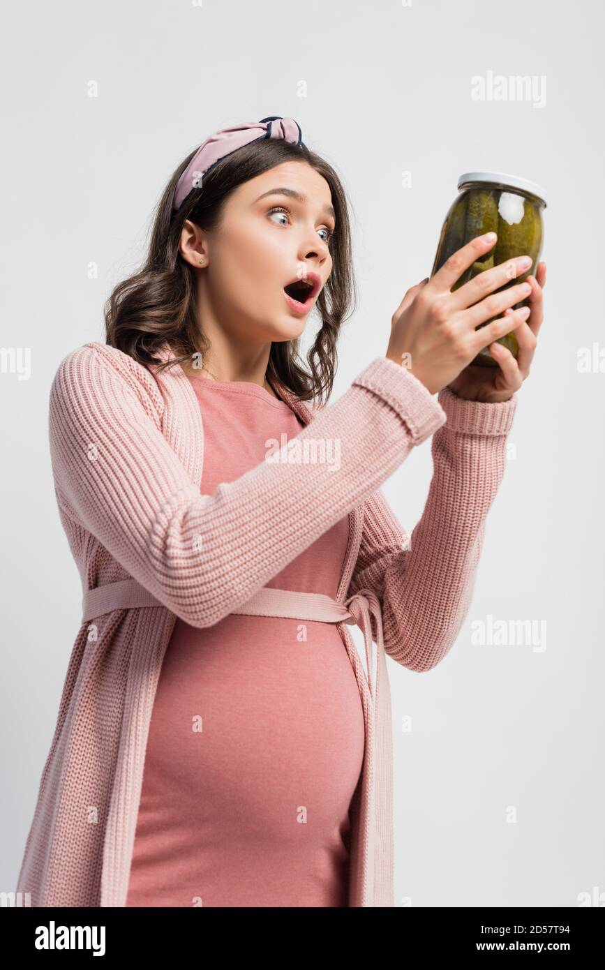 shocked and pregnant woman holding jar with pickled cucumbers isolated