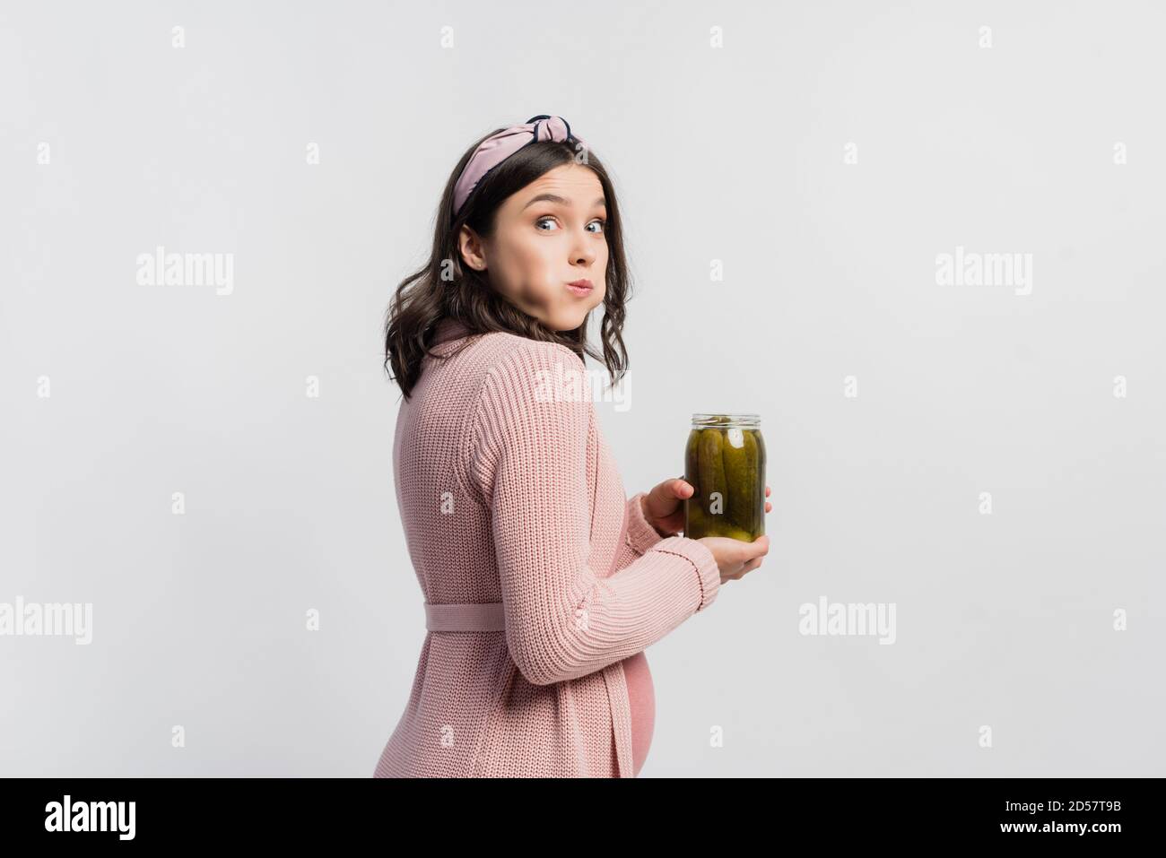 surprised and pregnant woman holding jar while eating pickled cucumbers