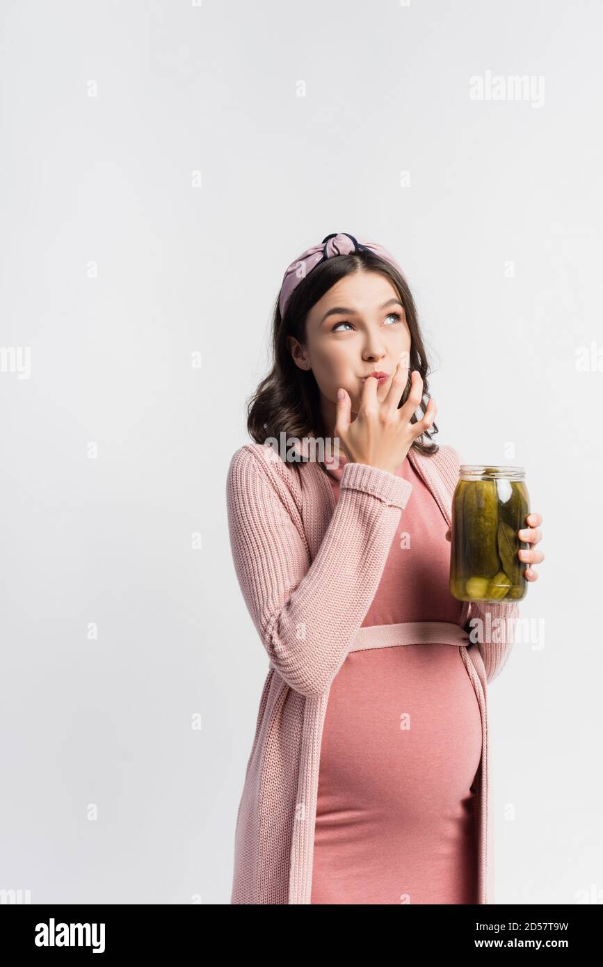 pregnant woman holding jar with pickled cucumbers while licking finger
