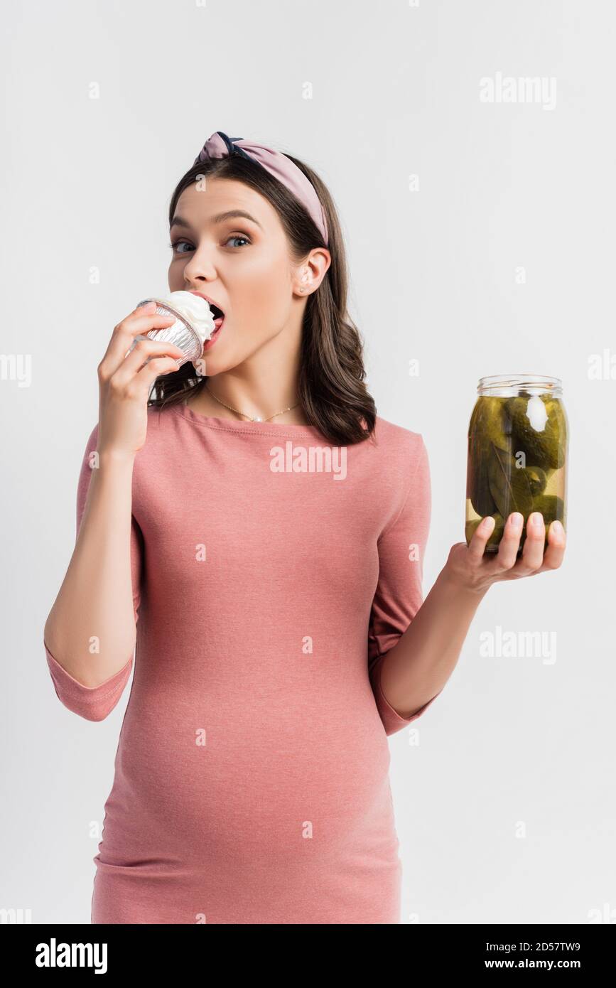 young pregnant woman eating cupcake and holding jar with pickled