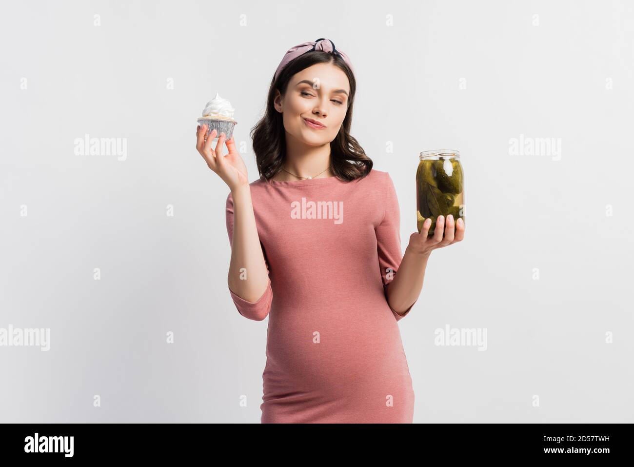 pregnant woman choosing between cupcake and jar with pickled cucumbers