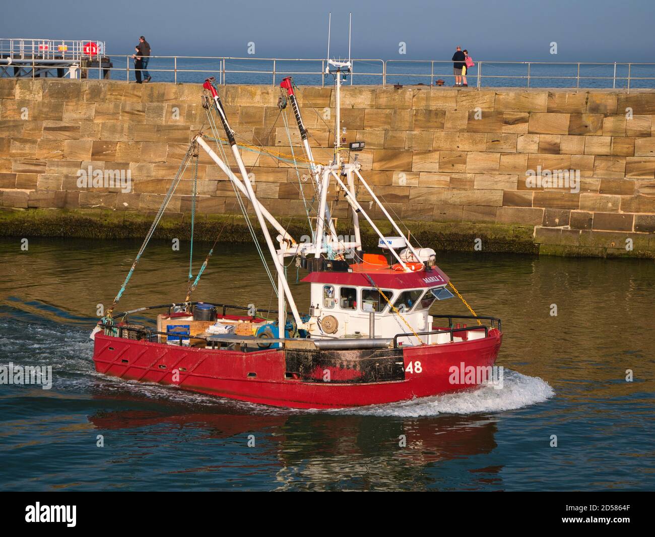 A red fishing boat returns to Whitby Harbour on the east coast of North Yorkshire, England, UK - taken at the end of the afternoon Stock Photo