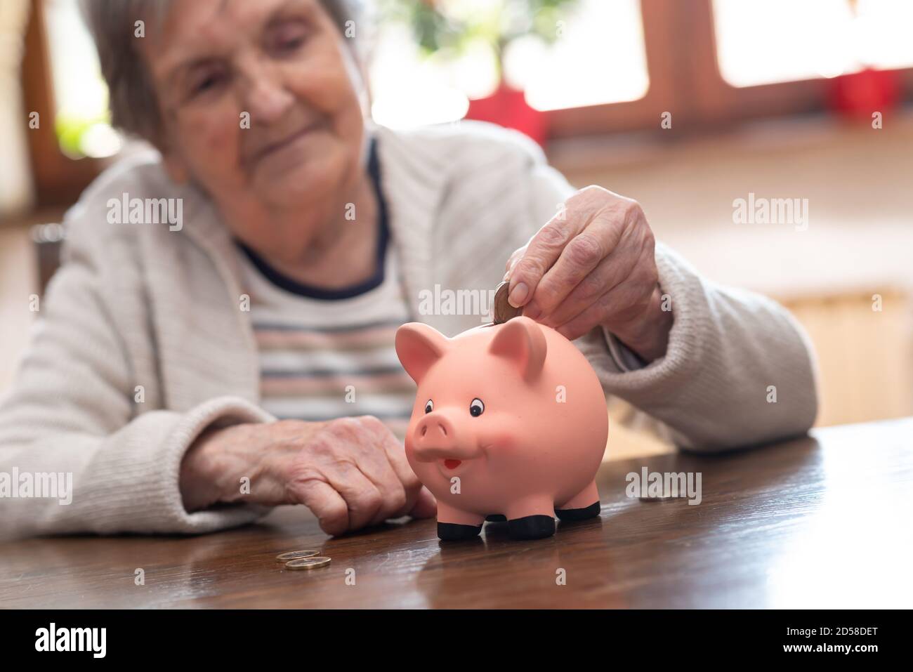 Elderly woman putting a coin in a piggy bank Stock Photo - Alamy