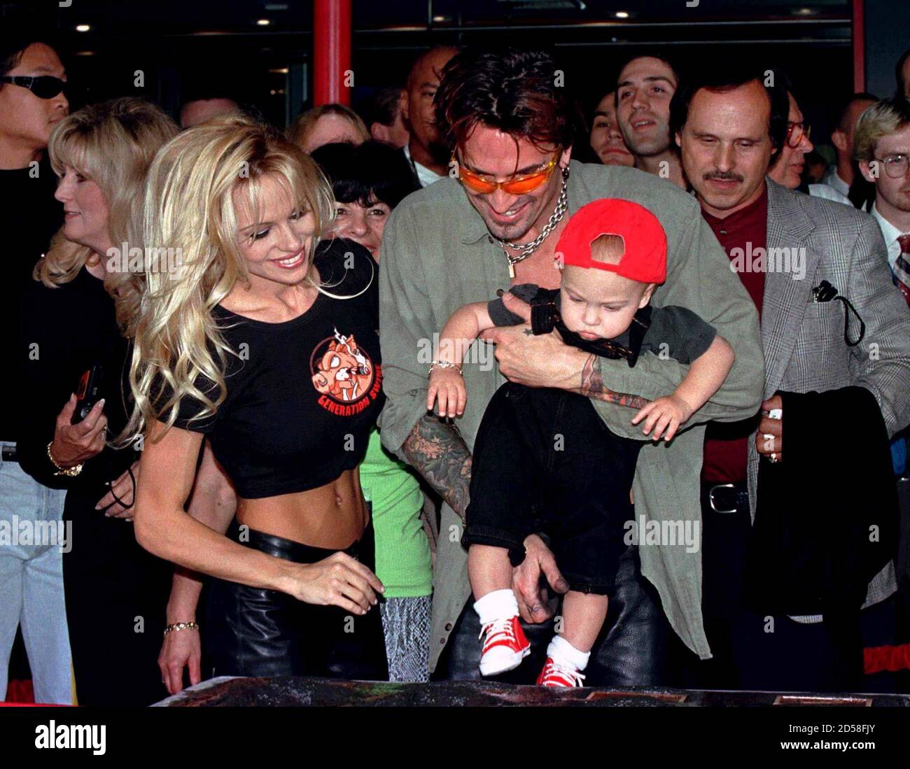 Actress Pamela Anderson Lee (L) looks on as husband, musician Tommy Lee  holds their son, Brandon Thomas Lee, above the cement plaque where Tommy  Lee's rock group 