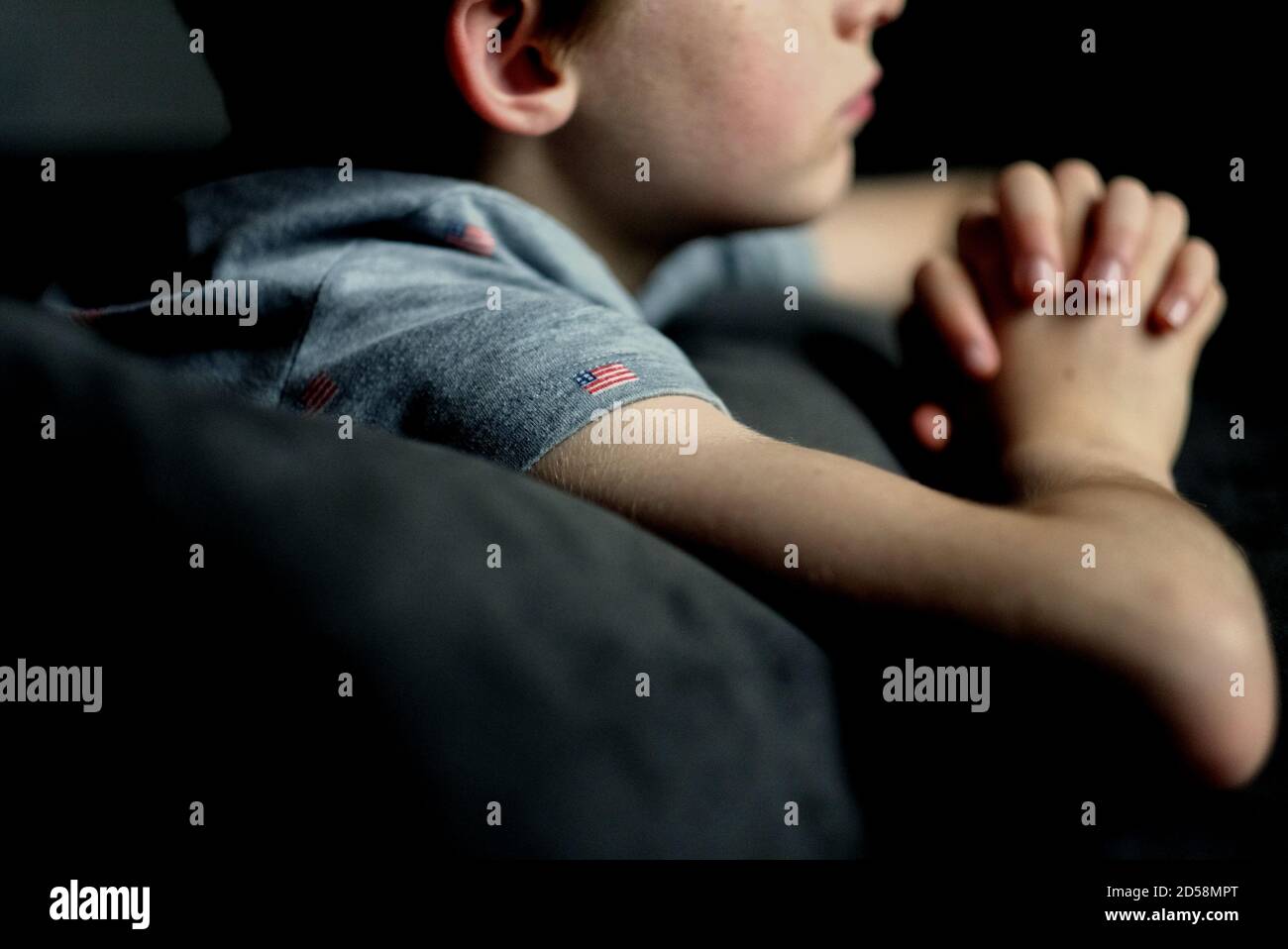 Close-up of a boy wearing an American flag t-shirt lying on his bed praying Stock Photo