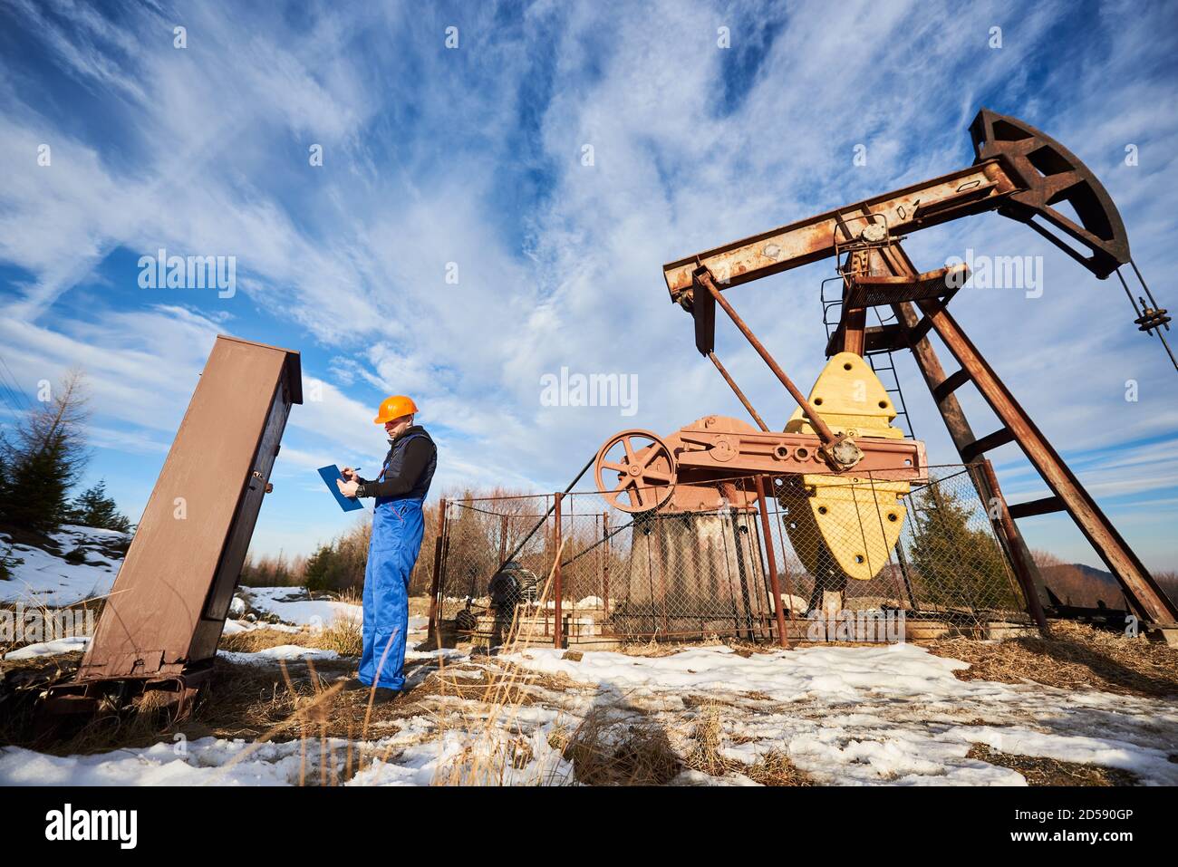 Petroleum engineer in work overalls and helmet making notes on