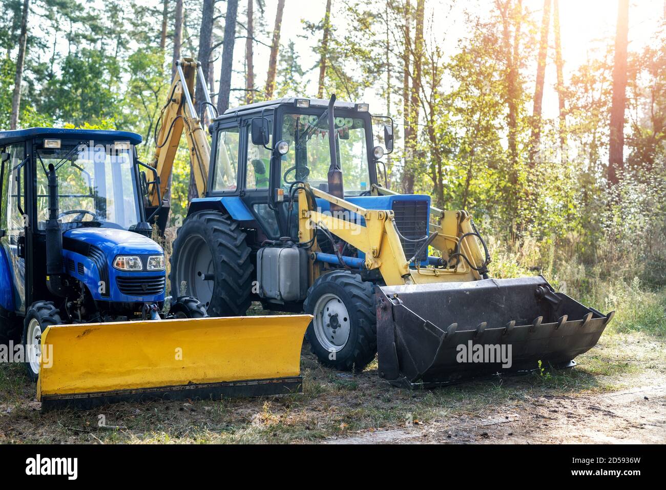 Two small and big modern tractors parked at backyard near forest farm at countryside