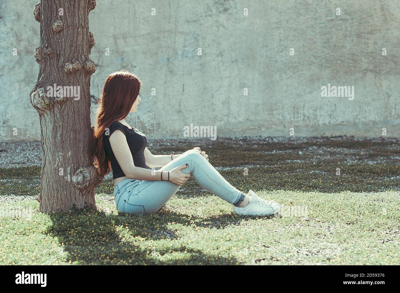 Teenager girl sitting in the garden leaning against a tree, Spain Stock Photo