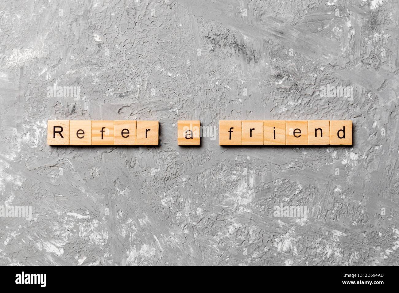 refer a friend word written on wood block. refer a friend text on table