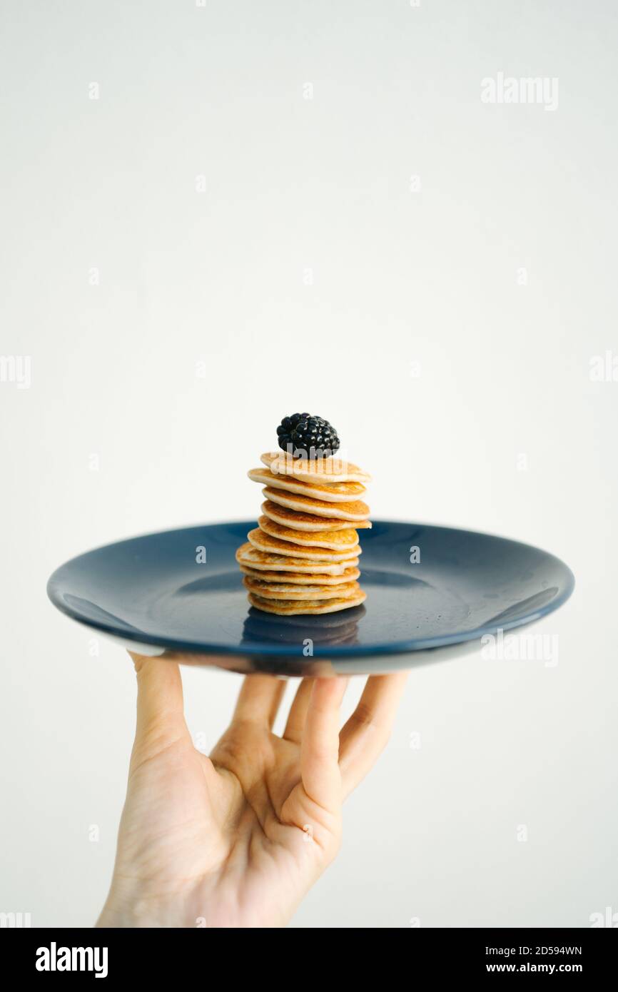 Man's hand holding a plate with a stack of miniature pancakes topped with blackberries Stock Photo