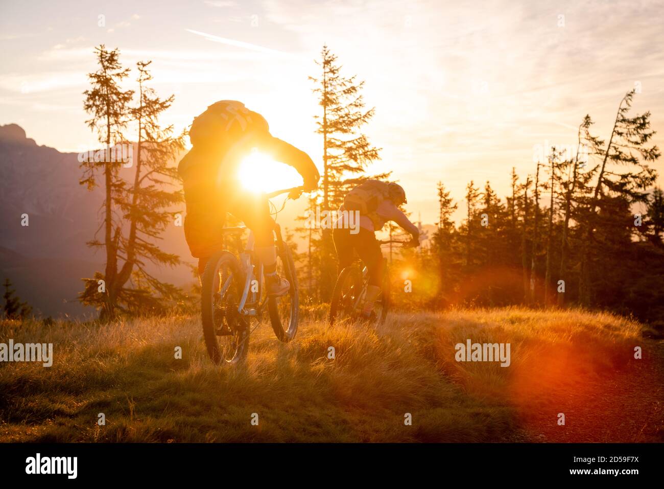 Rear view of two adults mountain biking in mountains at sunrise, Fadstadt, Salzburg, Austria Stock Photo