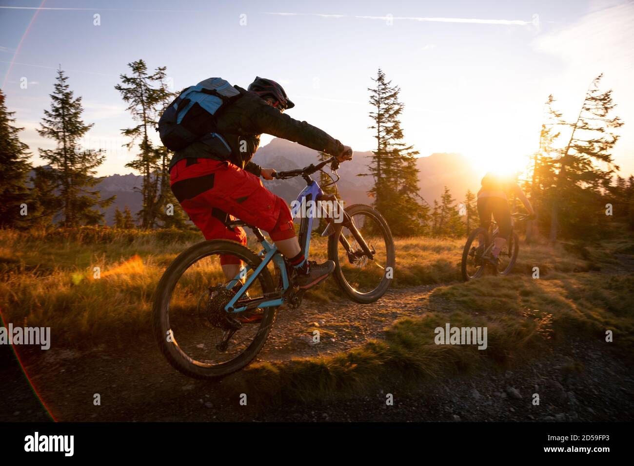 Rear view of two adults mountain biking in mountains at sunrise, Fadstadt, Salzburg, Austria Stock Photo