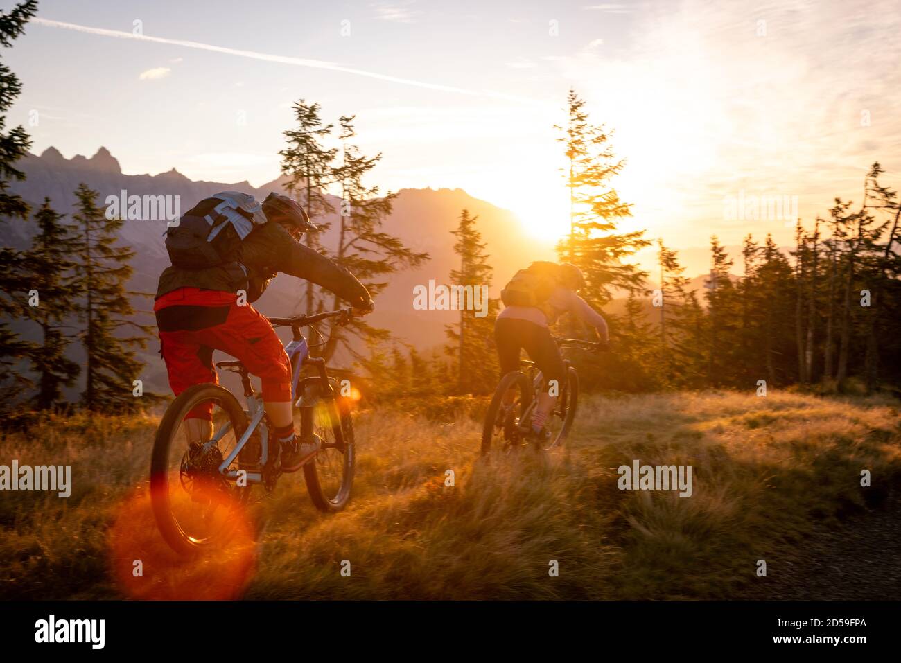 Rear view of two adults mountain biking in mountains at sunrise, Fadstadt, Salzburg, Austria Stock Photo