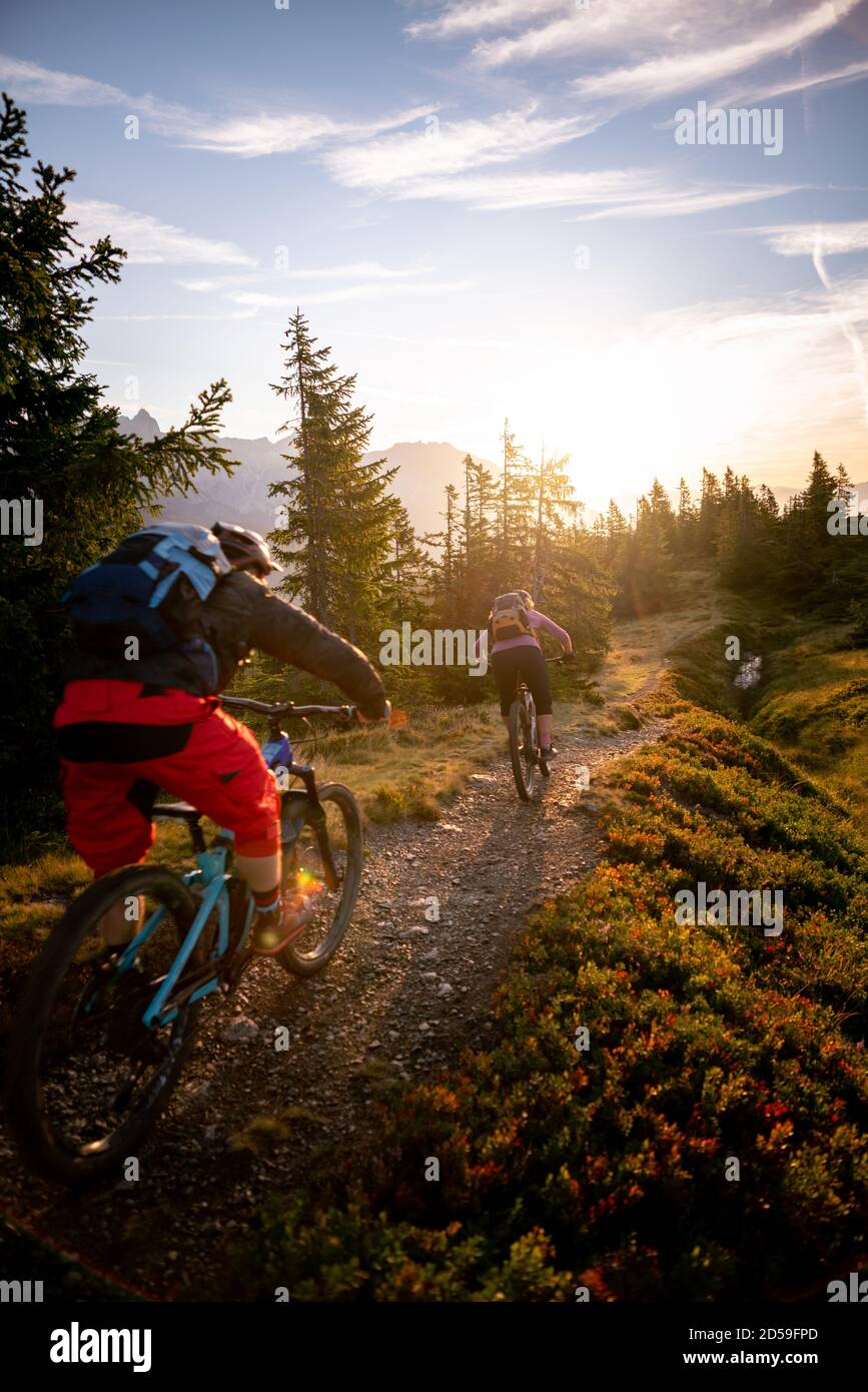 Rear view of two adults mountain biking in mountains at sunrise, Fadstadt, Salzburg, Austria Stock Photo