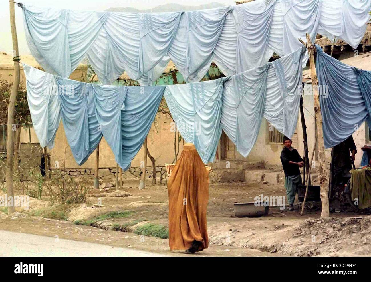 An Afghan woman wearing her burkha walks past a shop selling newly made burkhas in the Afghan capital, October 18. The Islamic Taliban militia who took Kabul three weeks ago, require women to be fully veiled when leaving the house. Stock Photo