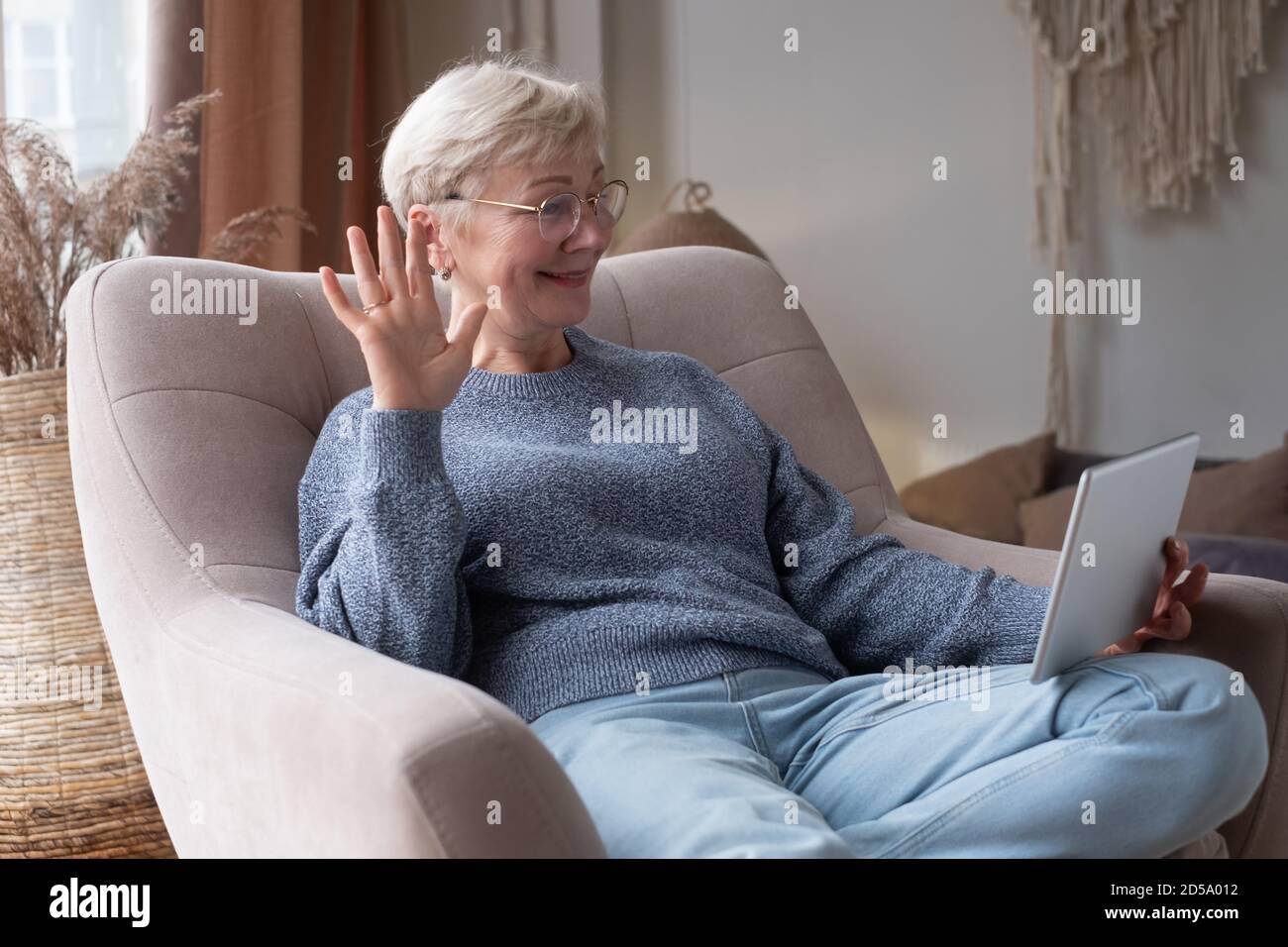 senior woman using tablet sitting at home chatting with friends Stock Photo