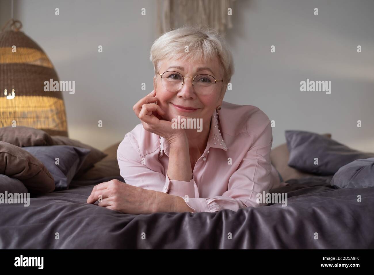 Senior caucasian woman relaxing on bed smiling at camera Stock Photo