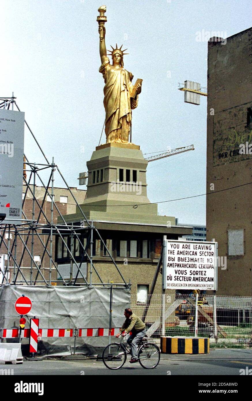 A cyclist passes a giant copy of the "Statue of Liberty ", May 29 which has been set up on top of a former east-German border guard watchtower at the former allied Checkpoint Charlie which is now a large construction site where U.S. investors build the American trade center. The sign reads in English, Russian, French and German " You are leaving the American sector Stock Photo