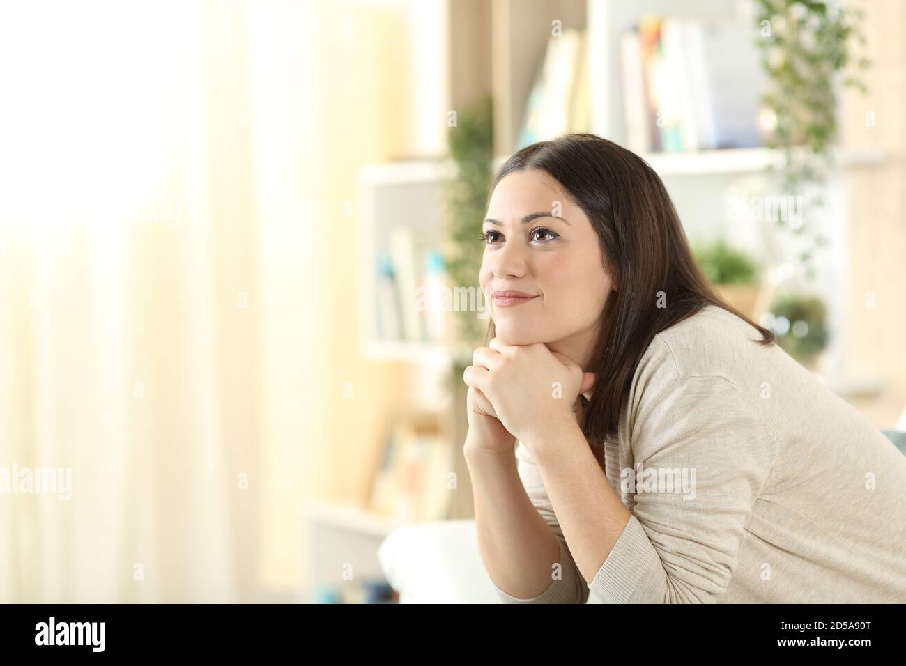 Pensive woman looks up dreaming sitting on a sofa at home Stock Photo