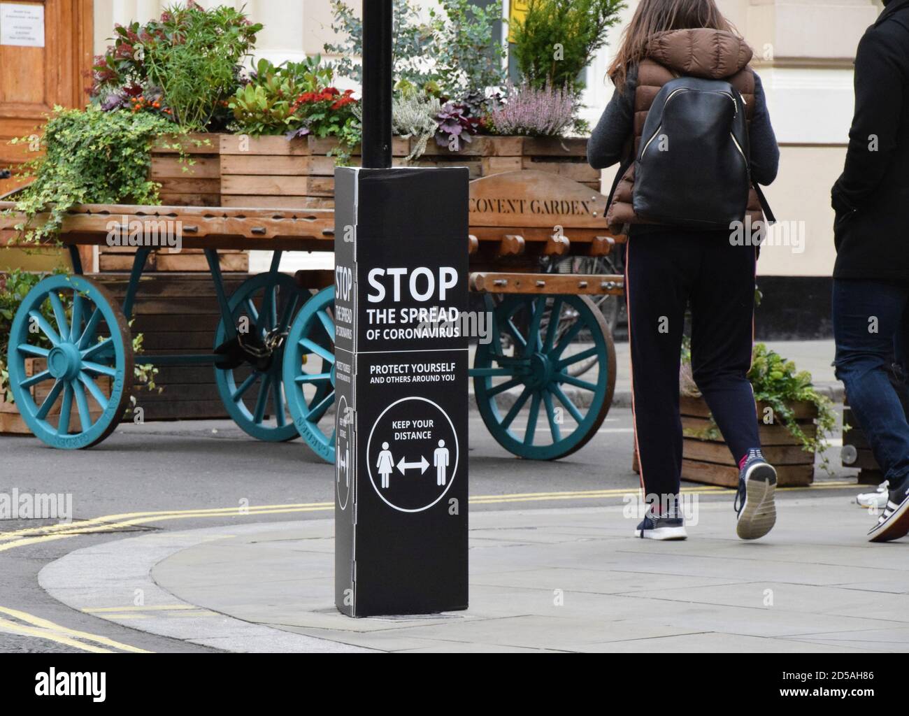 People walk past a Stop The Spread Of Coronavirus social distancing street sign in Covent Garden, London Stock Photo