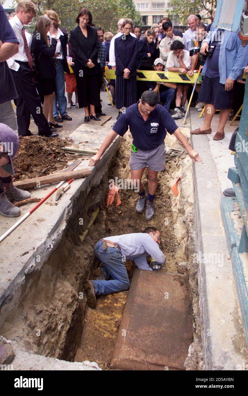 Archaeologist Peter Douglas uses a torch to look under a 196-year-old colonial gravestone in Sydney's business district March 31 as workers look-on during their lunch break. The headstone, discovered recently by builders on a city construction site, marks the grave of three-month-old William Kemp, the baby son of Captain Anthony Kemp one of colonial Australia's highest ranked military officers.  MDB/TAN Stock Photo