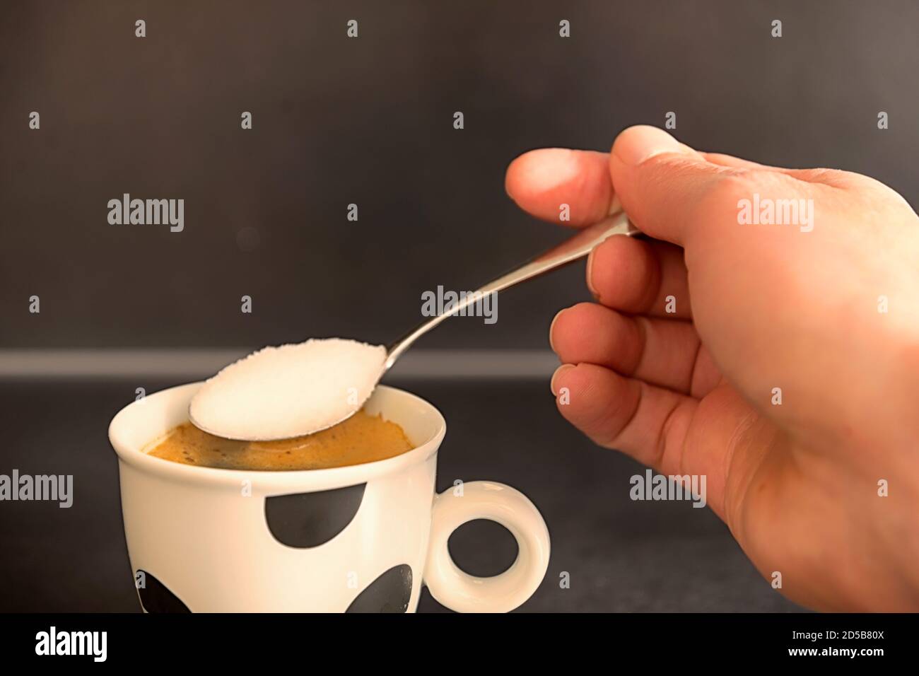 Hand holding a spoon, adding sugar to coffee. Stock Photo
