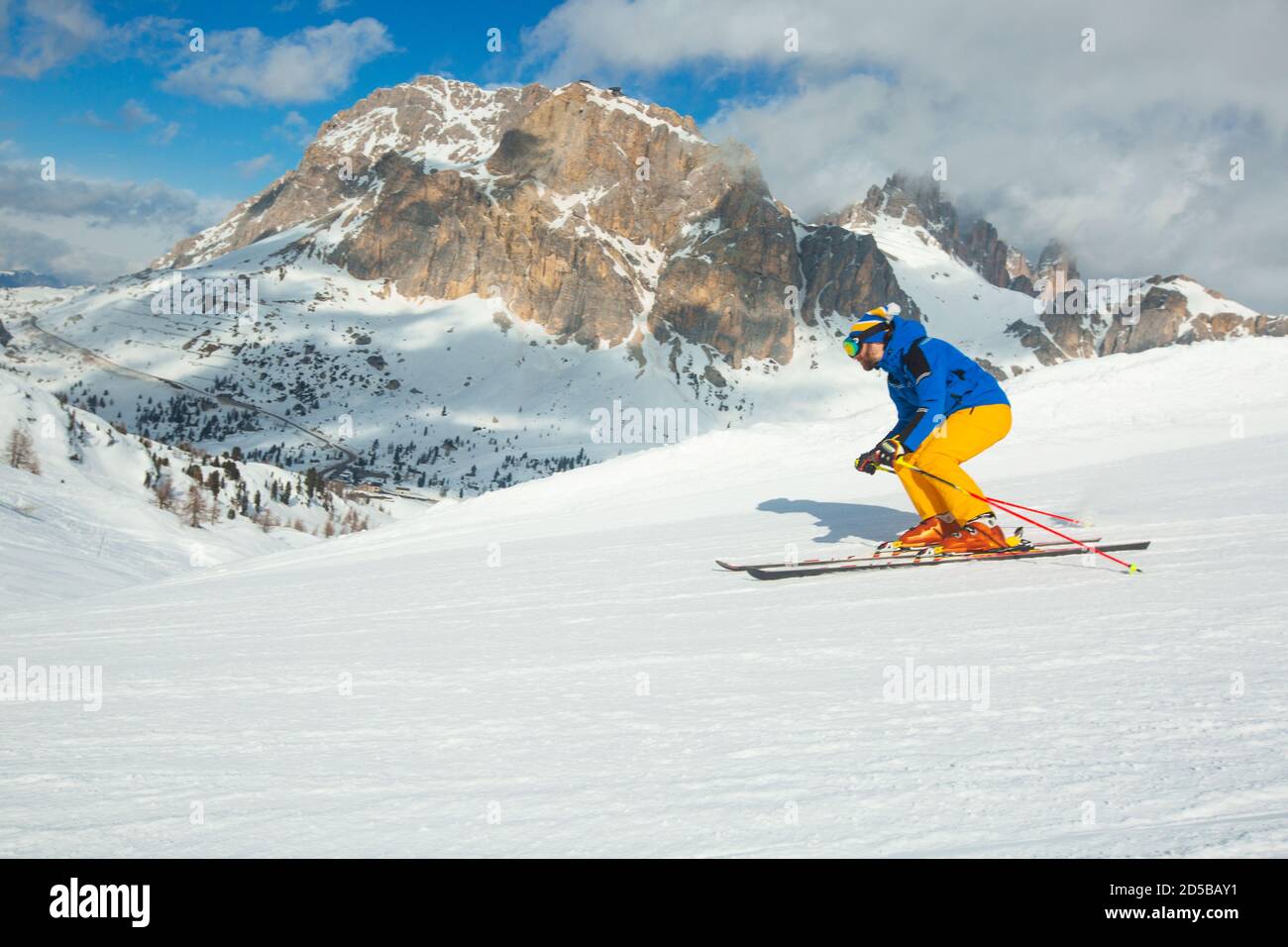 Male skier in blue and yellow clothes on slope with mountains in the background at Cortina d'Ampezzo Col Gallina Sella Ronda skiing resort area Dolomi Stock Photo