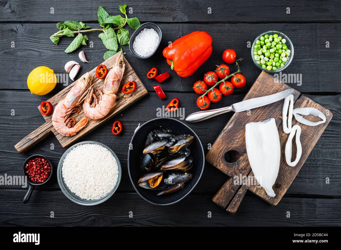 Fresh uncooked sea food specialties and rice with mussels, shrimps and squid on black wooden background, flat lay Stock Photo