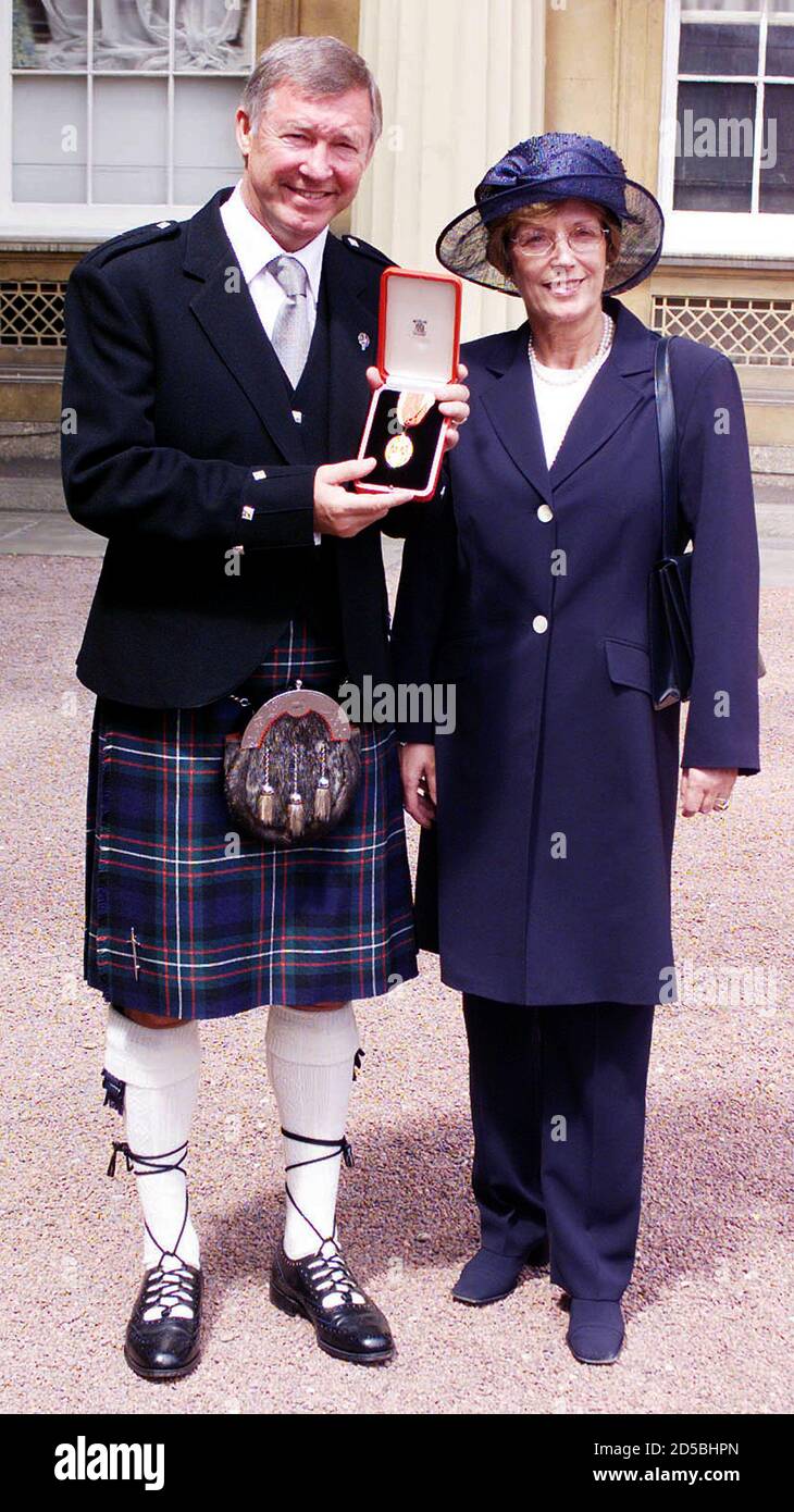 Manchester United manager Sir Alex Ferguson and wife Cathy pose for  photographs July 20, 1999. Ferguson was knighted by Britain's Queen  Elizabeth II during an investiture ceremony at Buckingham Palace.  REUTERS/Pool PS/GB