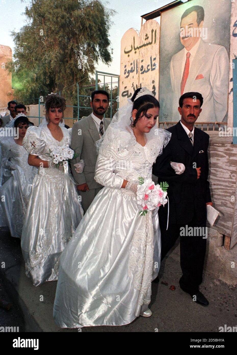 Brides and grooms walk past a portrait of Iraqi President Saddam Hussein August 9. Some 112 couples got married on Monday in an event prepared and paid for by the Iraqi youth Association, a body chaired by President Saddam Hussein's elder son.  FK/ME Stock Photo