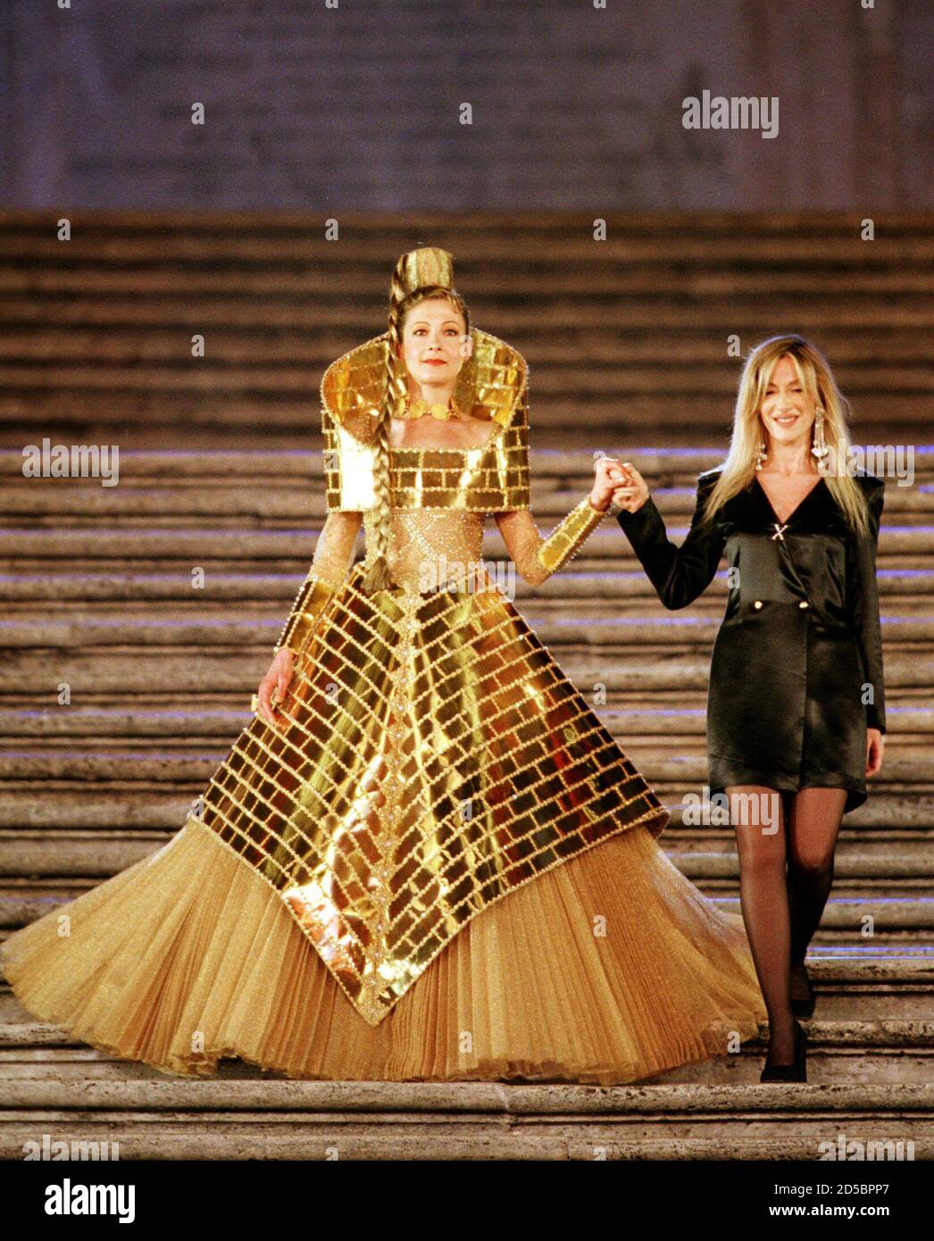 American model Deborah Moore (L) wears a dress made of gold by Italian designer Alexandra Fede (R) as part of her autumn/winter '99 collection during a fashion extravaganza gala at Rome's Spanish Steps which ended  Rome's high fashion week July 16. Some thirty fashion houses took part in  the show. Stock Photo